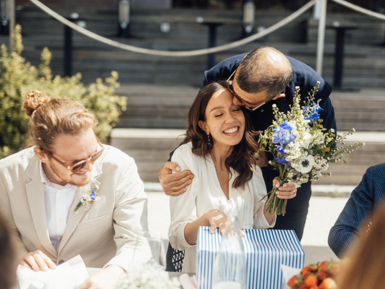 Bride receiving kiss on the head from family member while opening gifts at wedding