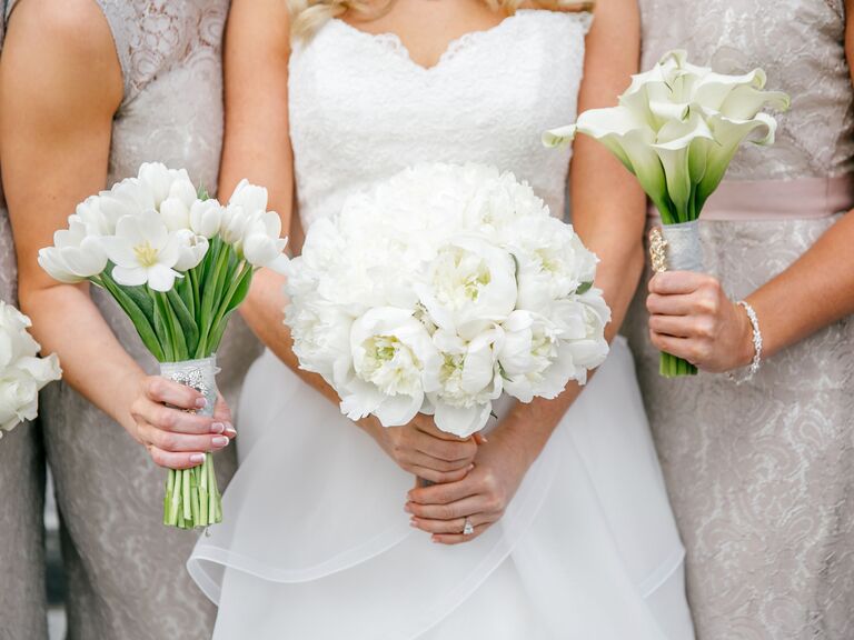 A bride holds a bouquet of white peonies, while her bridesmaids flank her holding complementary white flowers.