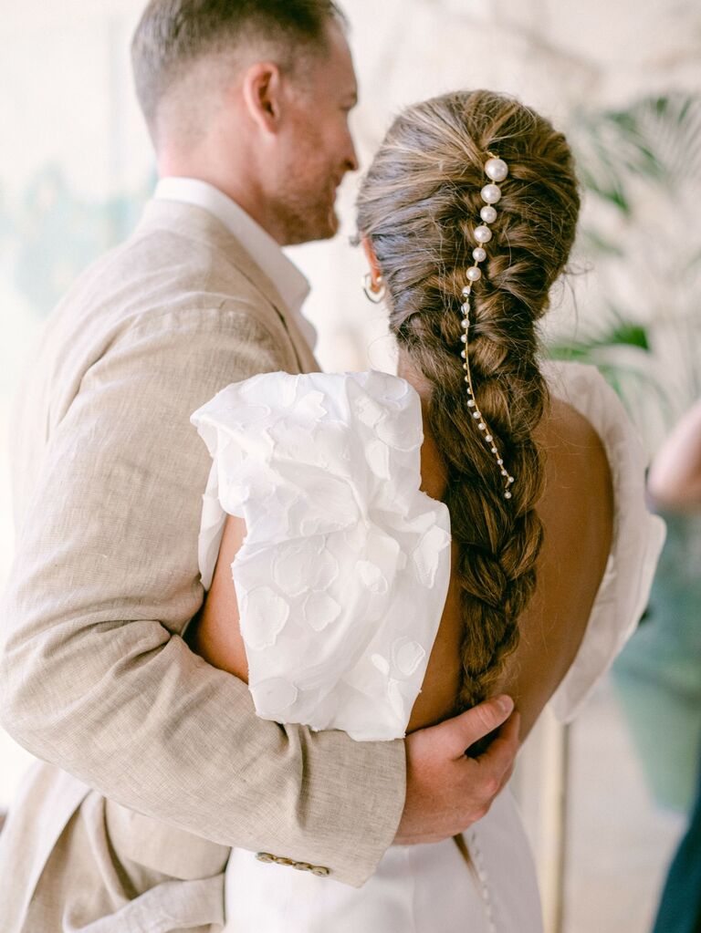 Bride wears her hair in a long braid embellished with pearl accents. 