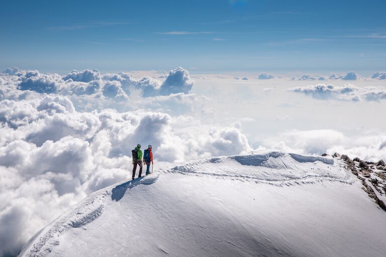 A couple walking on a snowy mountain above the clouds in Switzerland
