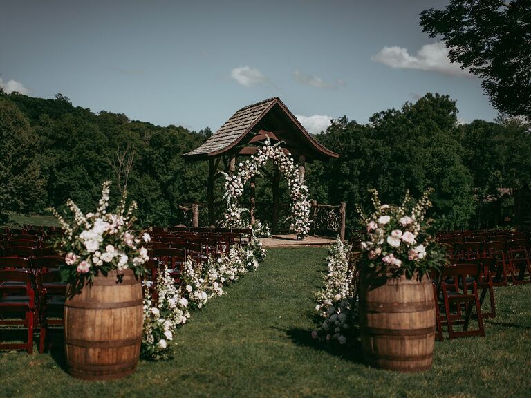 Outdoor ceremony space with decorative barrels, florals and wooden arch