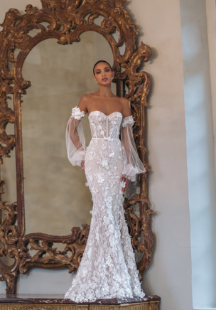 Individually hand beaded for more than 80 hours the embellishment scatters through the dress organically adding the feeling of flow and movement. Karter, an extravagant fitted wedding gown, is as striking as it is sexy. Decorated with oversized exclusive floral lace this bridal gown will undoubtedly stun. In a creamy neutral palette, this strapless dress features a deeply plunged sweetheart corset and sheer lantern sleeves that can be taken off. Accessorized with a lush Tulle overskirt , it takes on extra volume for a chic and elegant bridal look.