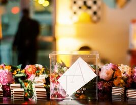 Transperant wedding gift box sits on a table surrounded by beautiful florals. 