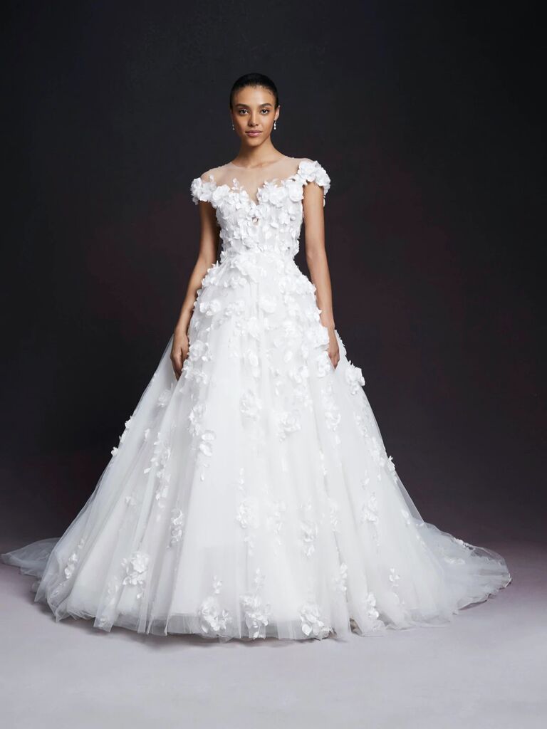 bride stands against black backdrop wearing ball gown wedding dress with floral 3D embellishments