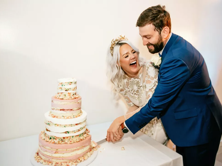 A bride and groom laugh as they cut their wedding cake