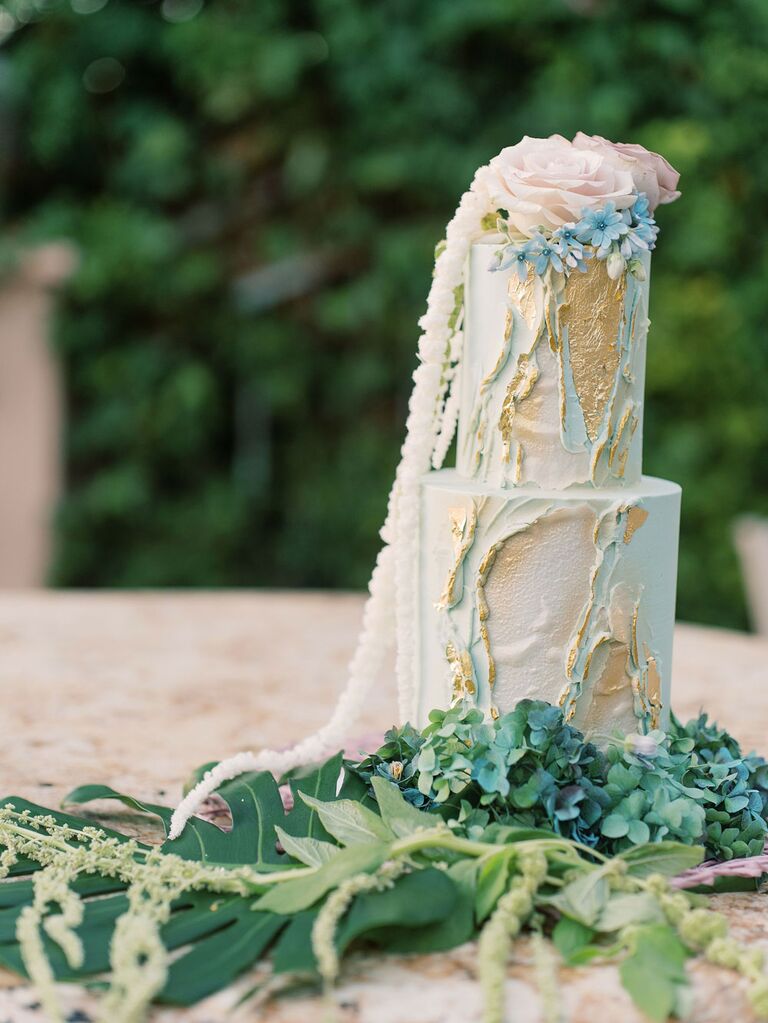 Ethereal blue and gold beach wedding cake on bed of greenery