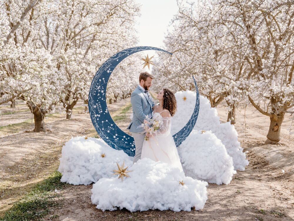 Bride and groom at celestial wedding posing in front of crescent moon with 3D cloud puffs