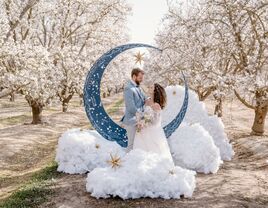 Bride and groom at celestial wedding posing in front of crescent moon with 3D cloud puffs