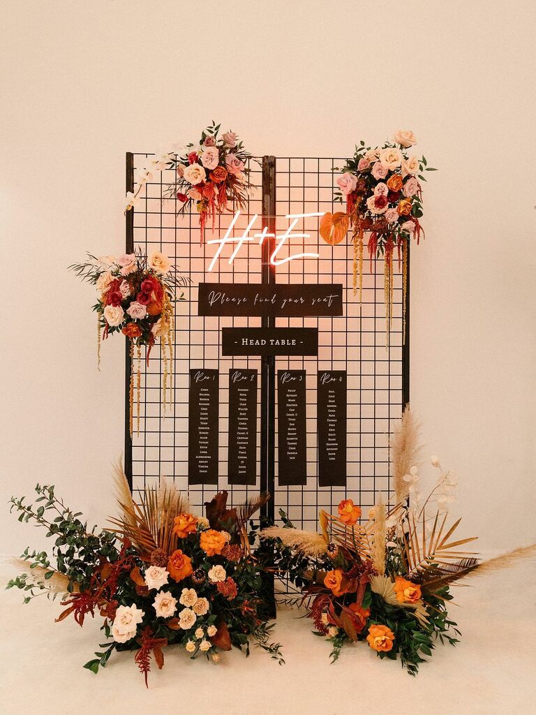 Black seating chart with neon sign and colorful flowers