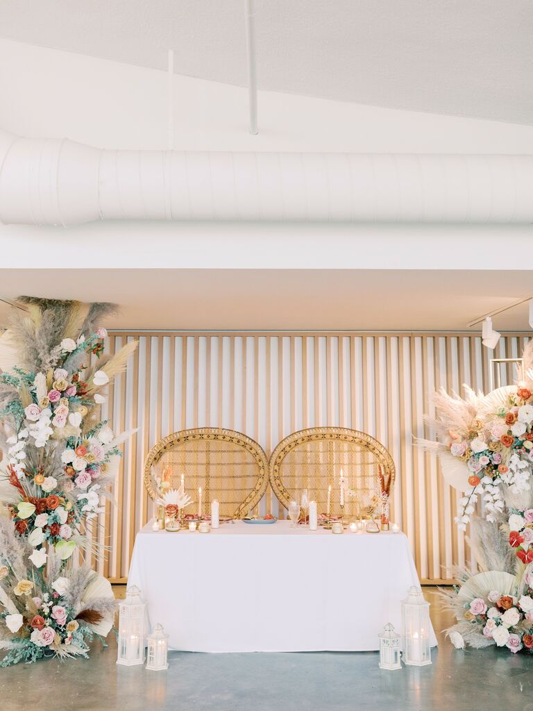 boho wedding sweetheart table decor with rattan peacock chairs and floor-to-ceiling flower pillars with pampas grass