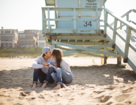 Couple kissing on beach in Orange County, California in front of lifeguard stand