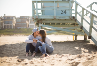 Couple kissing on beach in Orange County, California in front of lifeguard stand