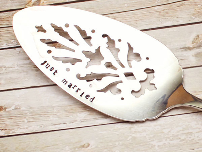 Silver cake server with intricate cutouts and 'just married' in typewriter font on side