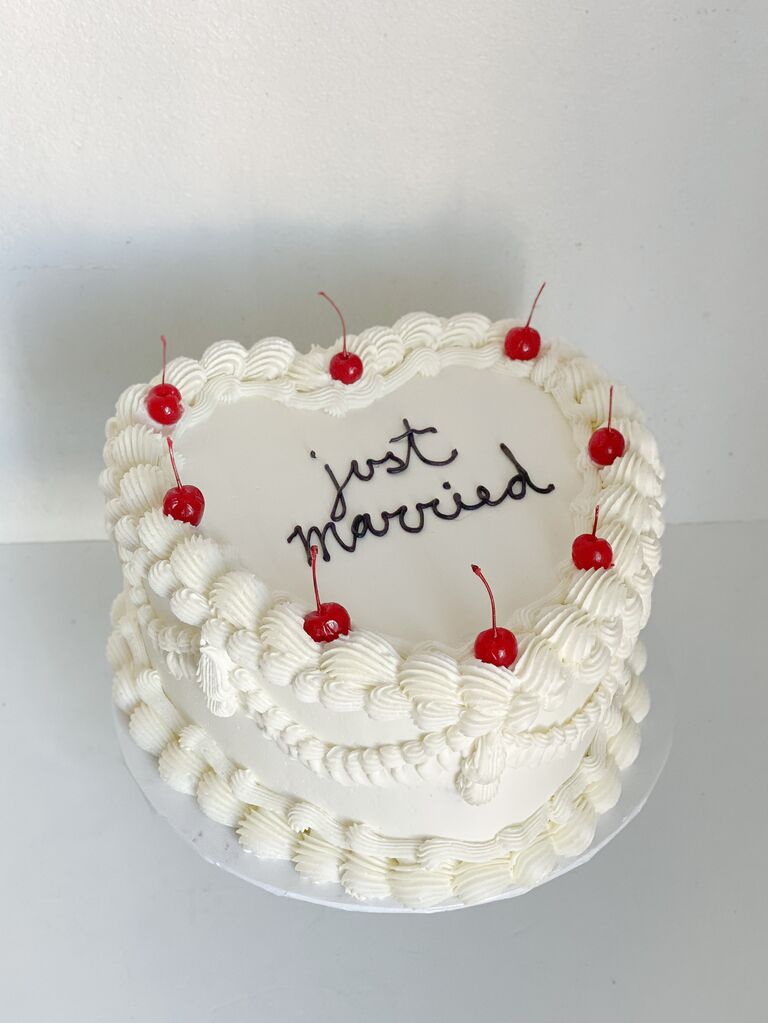simple heart shaped wedding cake with just married written in black piping on white icing decorated with cherries