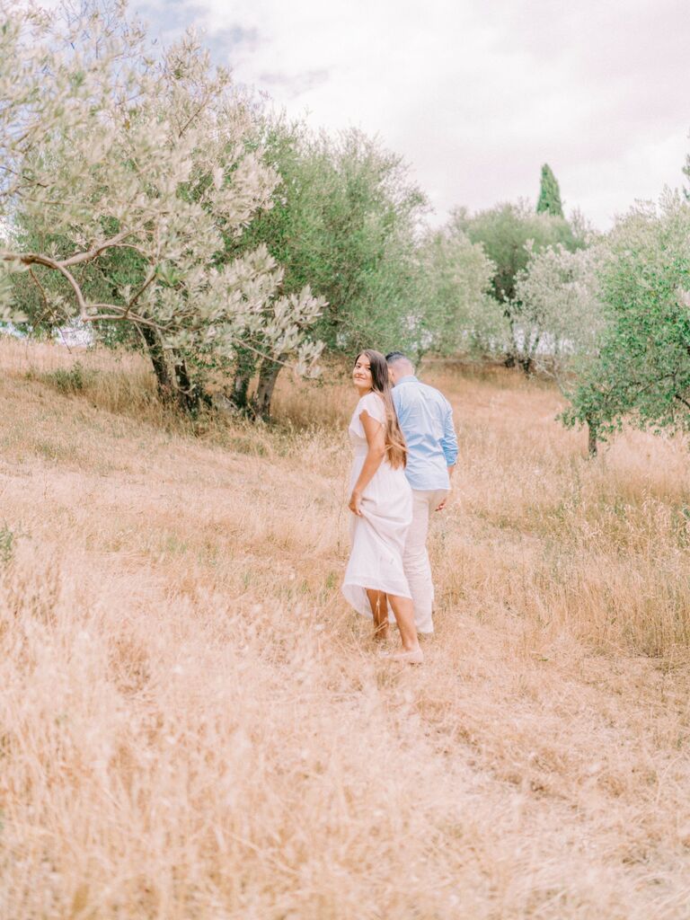 Woman looks back at the photographer while her and her husband walk throw a field. 