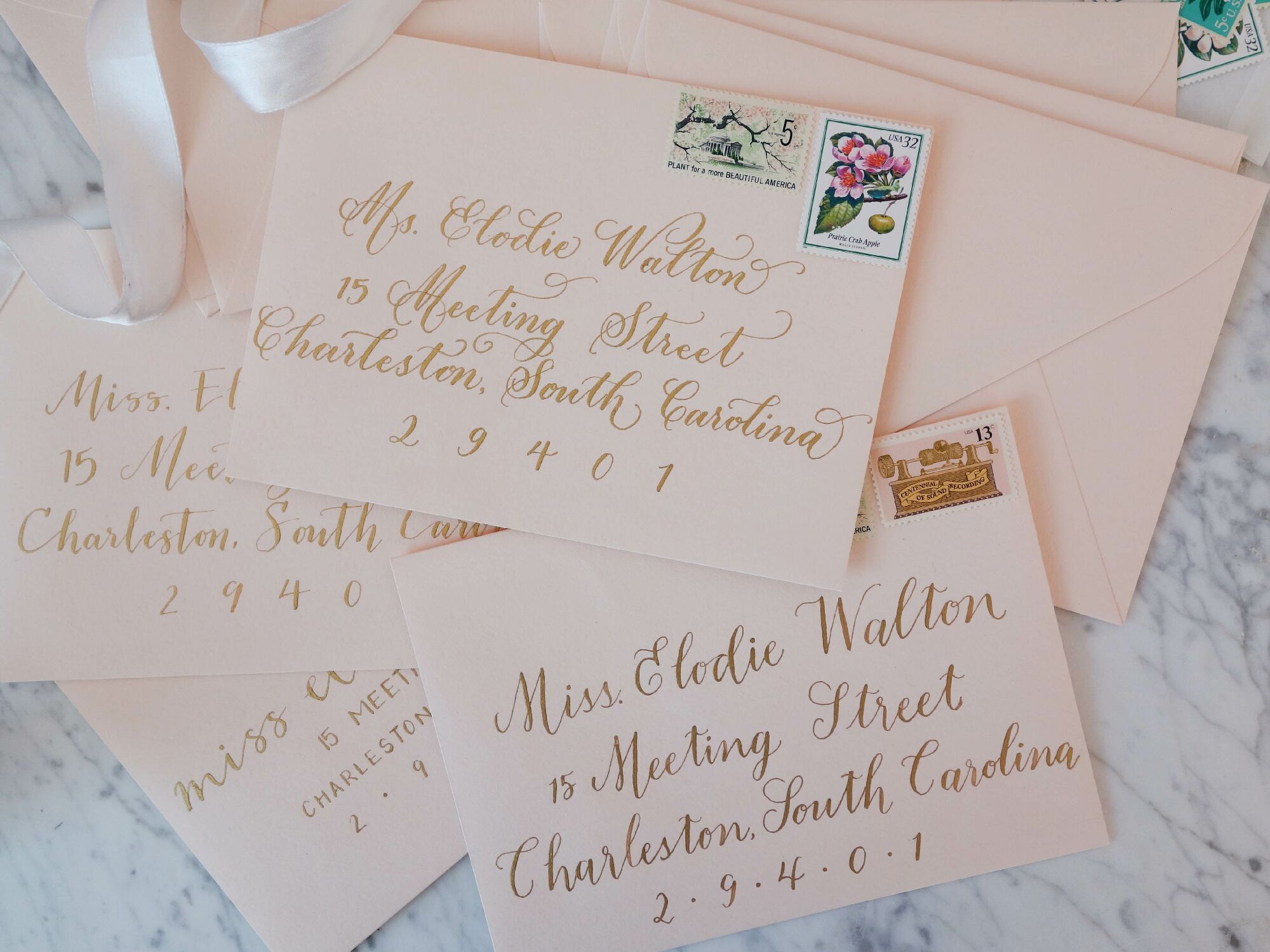 Stack of blush pink envelopes with gold calligraphy addresses