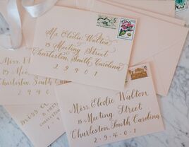 Stack of blush pink envelopes with gold calligraphy addresses