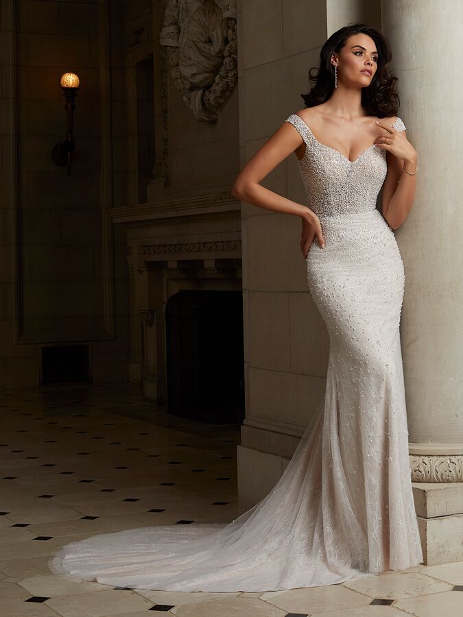 model stands against stone column wearing beaded fit and flare wedding dress