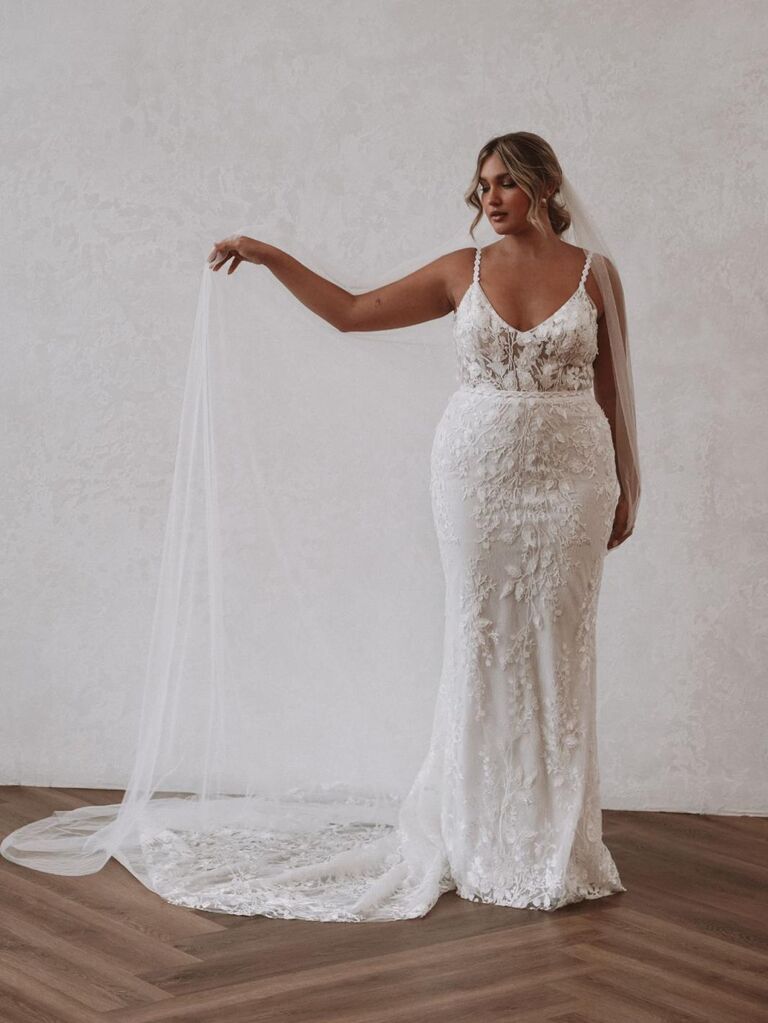 Model wears an elegant wedding dress with floral detailing. 