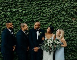 A groom poses with his bride and wedding party, leaning in for a laugh with his best man.