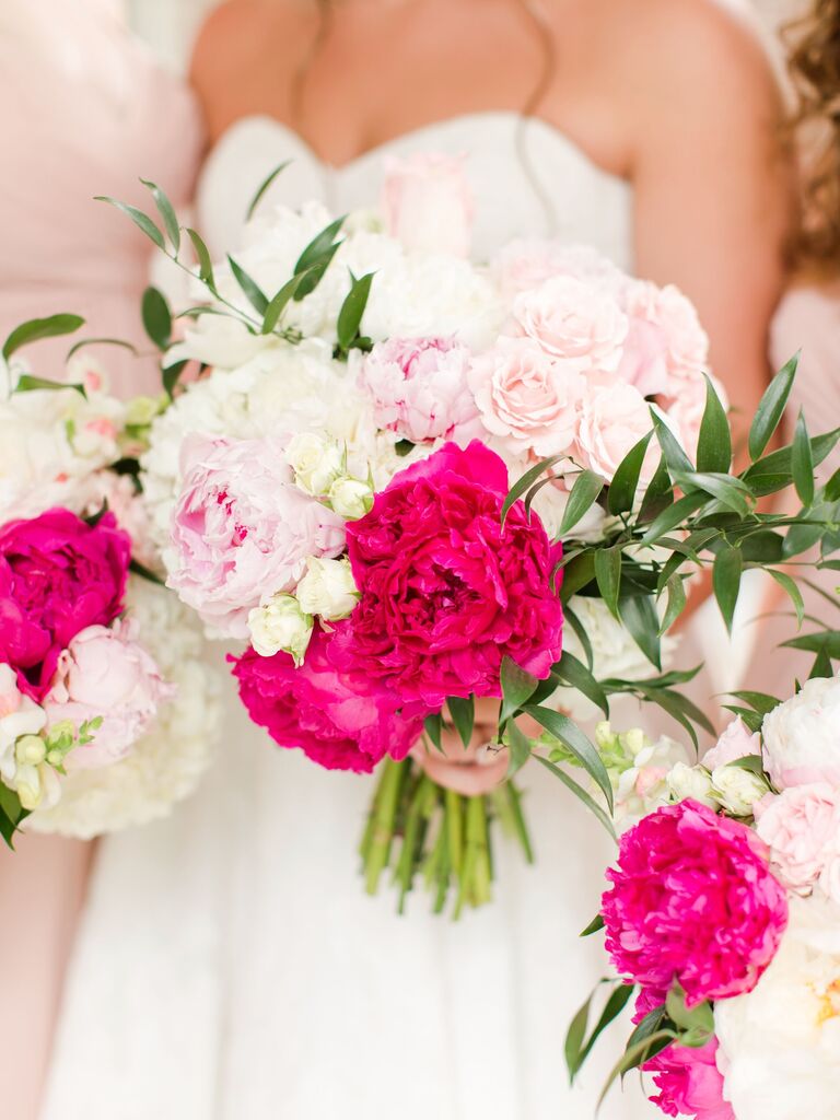 A bride holds an overflowing bouquet of hot pink and white peonies.