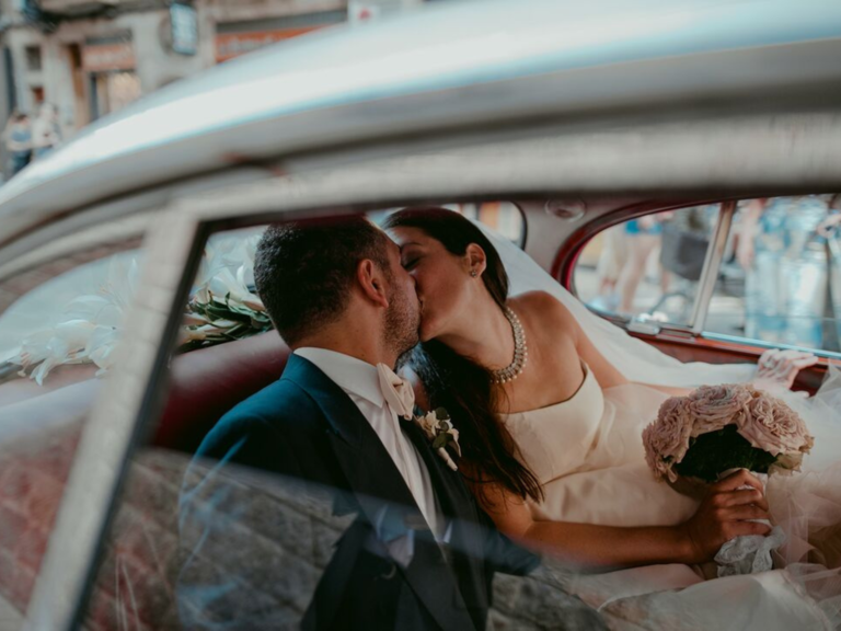 Bride and groom kissing in the back of car on wedding day