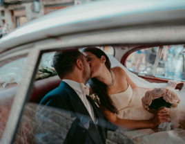 Bride and groom kissing in the back of car on wedding day