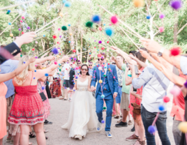 Wedding guest holding up multicolored pom poms as bride and groom walk through tunnel, Peruvian wedding traditions