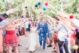 Wedding guest holding up multicolored pom poms as bride and groom walk through tunnel, Peruvian wedding traditions