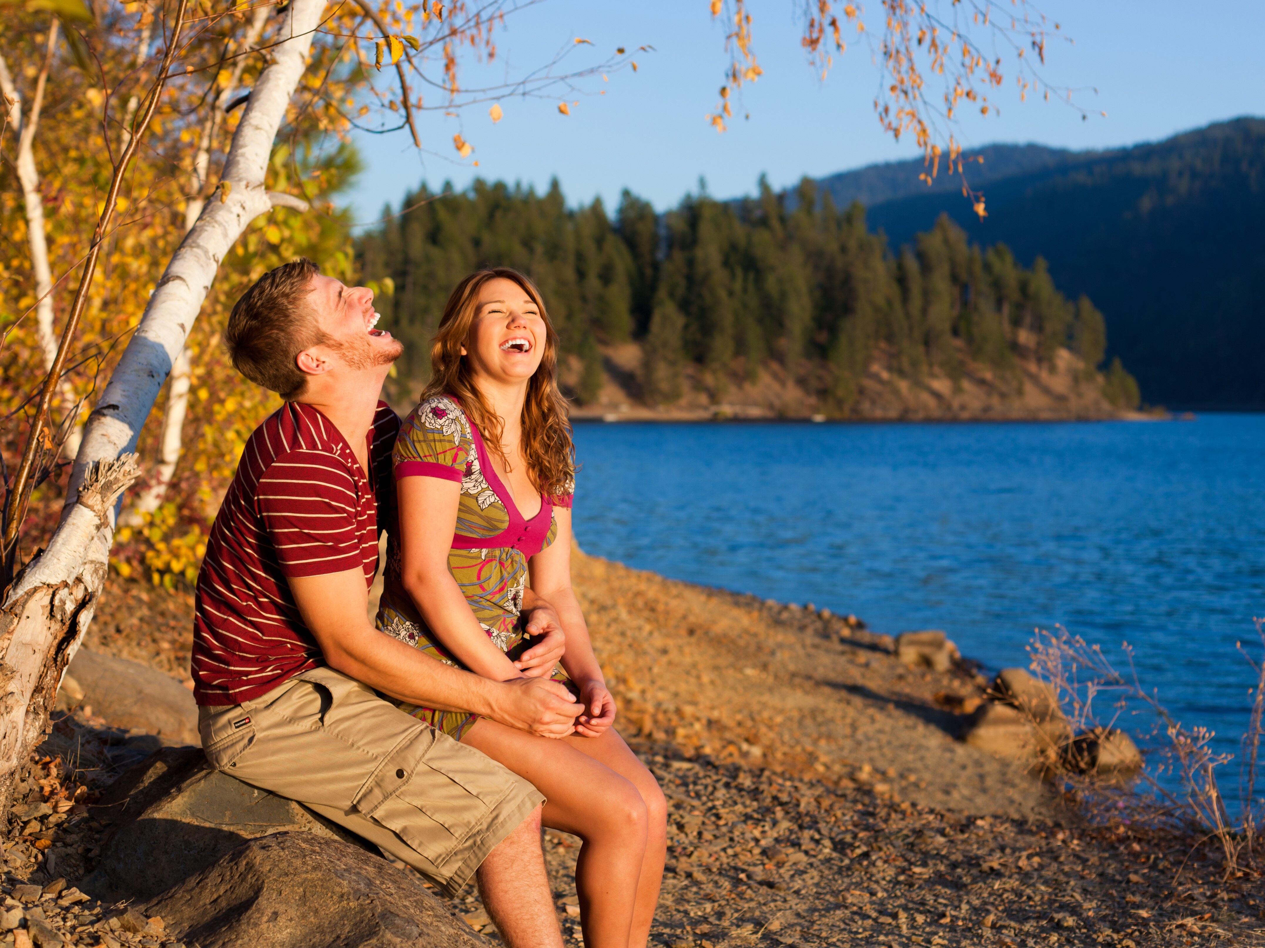 Happy couple laughing while sitting beside a lake and mountains