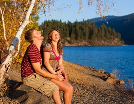 Happy couple laughing while sitting beside a lake and mountains