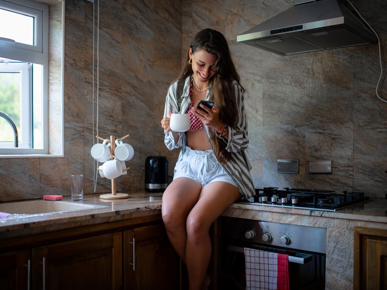 Woman sitting on her kitchen worktop while looking at her phone