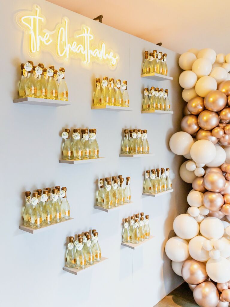 trendy wedding favor display with mini bottles of champagne on wall with yellow neon sign 