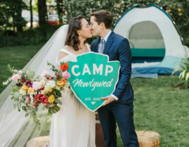 Couple kissing while holding camping-themed sign