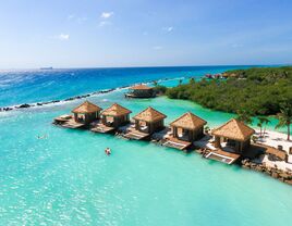 beautiful bungalows jut out to sea in aruba against multiple colors of blue waters