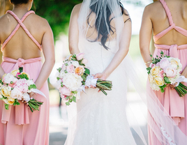 Bride and bridesmaids holding colorful bouquets with their backs turned to the camera.