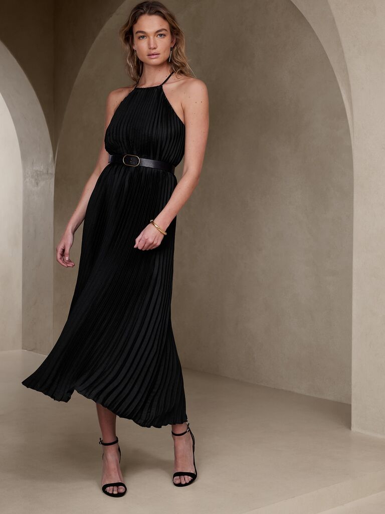 Model wears a black pleated dress with a halter neckline. 