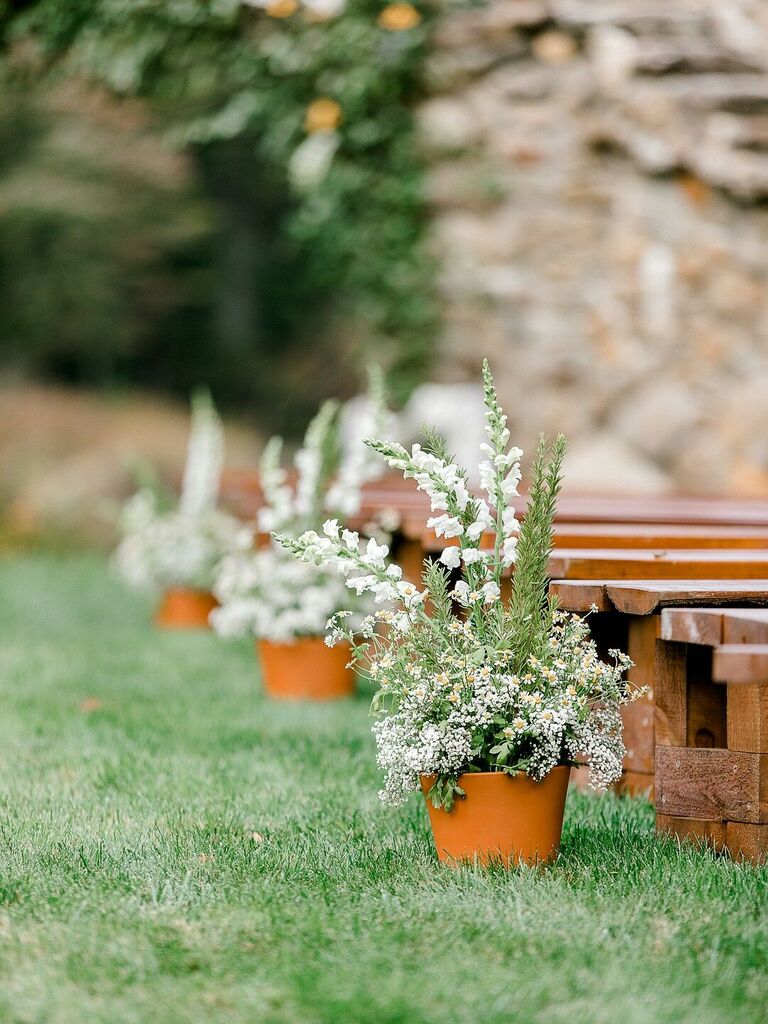 outdoor wedding ceremony aisle with low wooden benches and white flowers in terracotta pots as aisle markers
