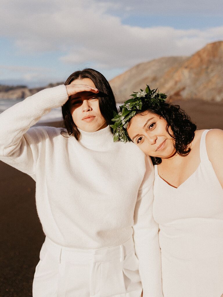 Brides wearing white sweater and pants and white slip dress on beach