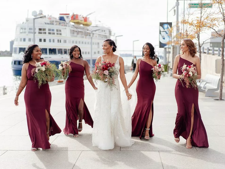 A bride walks with her wedding party along the docks with a boat in the background.