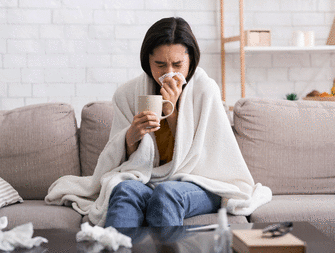 Woman blowing into a napkin and holding a cup of tea because she's sick.