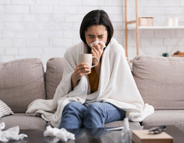 Woman blowing into a napkin and holding a cup of tea because she's sick.