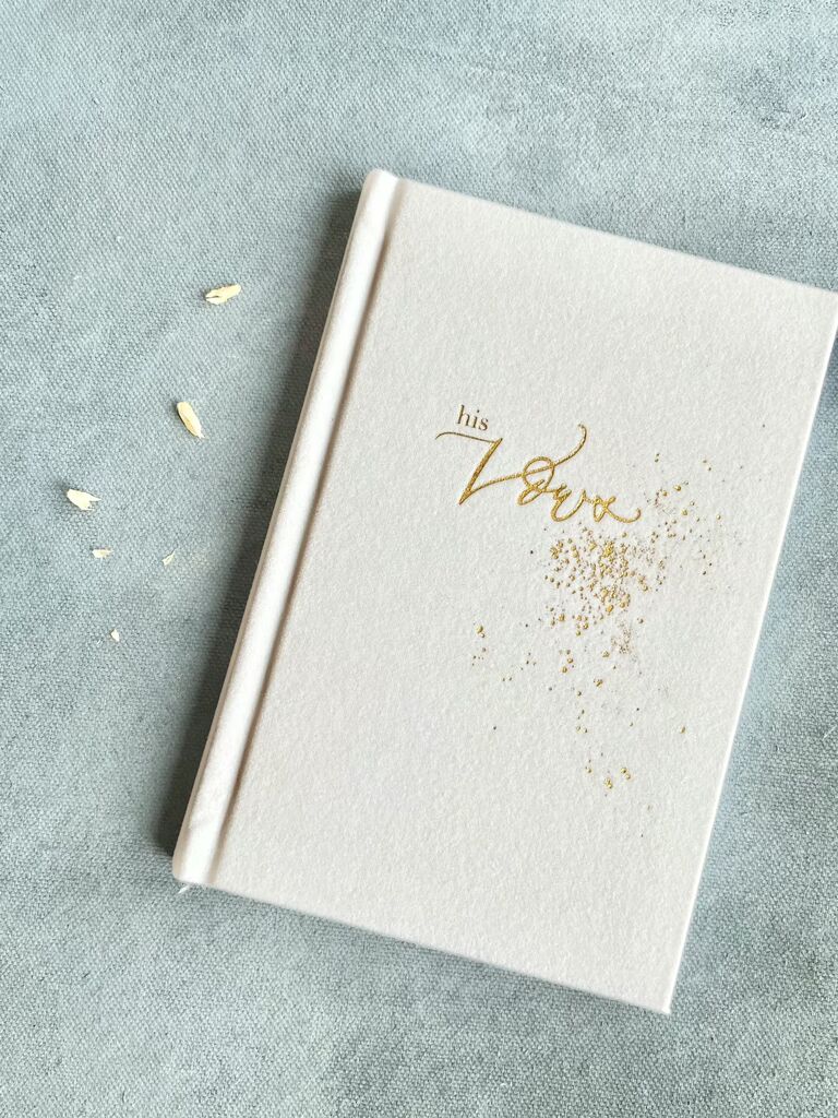 ivory velvet wedding vow book embossed with his vows written in gold lettering