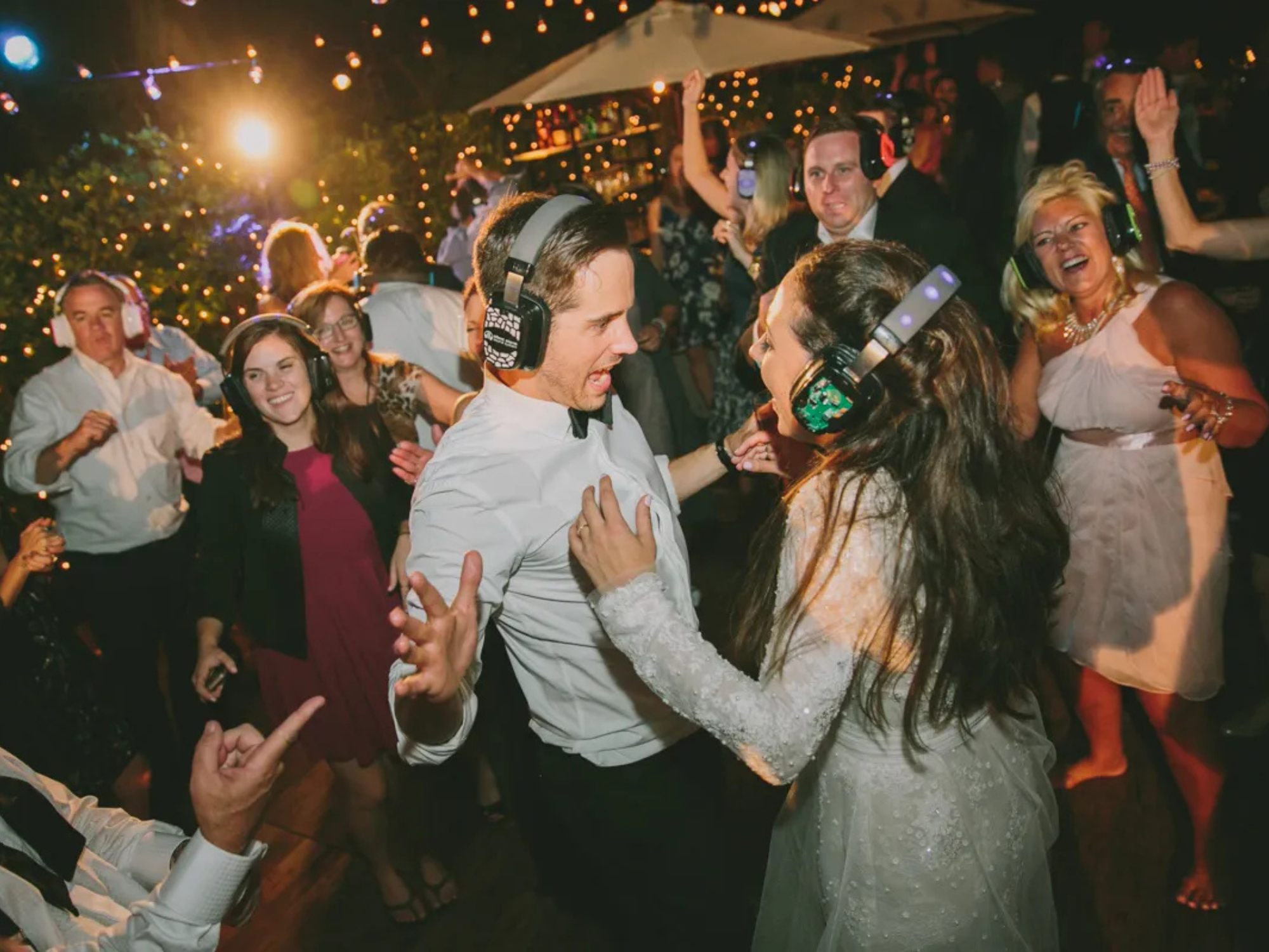 Bride, groom and wedding guests dancing with headphones at silent disco reception