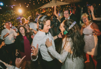 Bride, groom and wedding guests dancing with headphones at silent disco reception