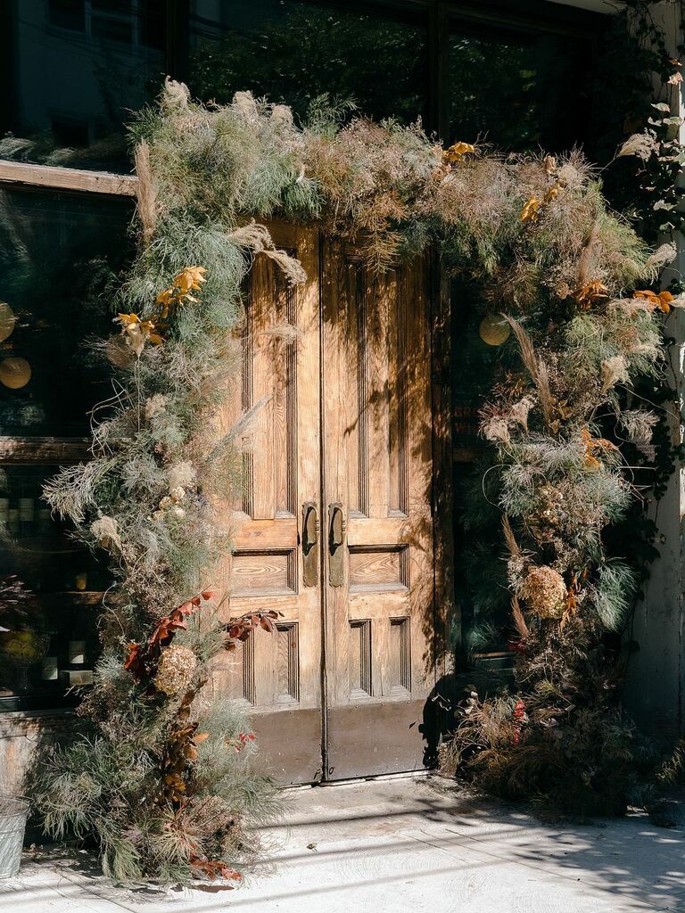 exterior wedding venue entrance with wooden double doors decorated with dried grasses and dried brown leaves on branches