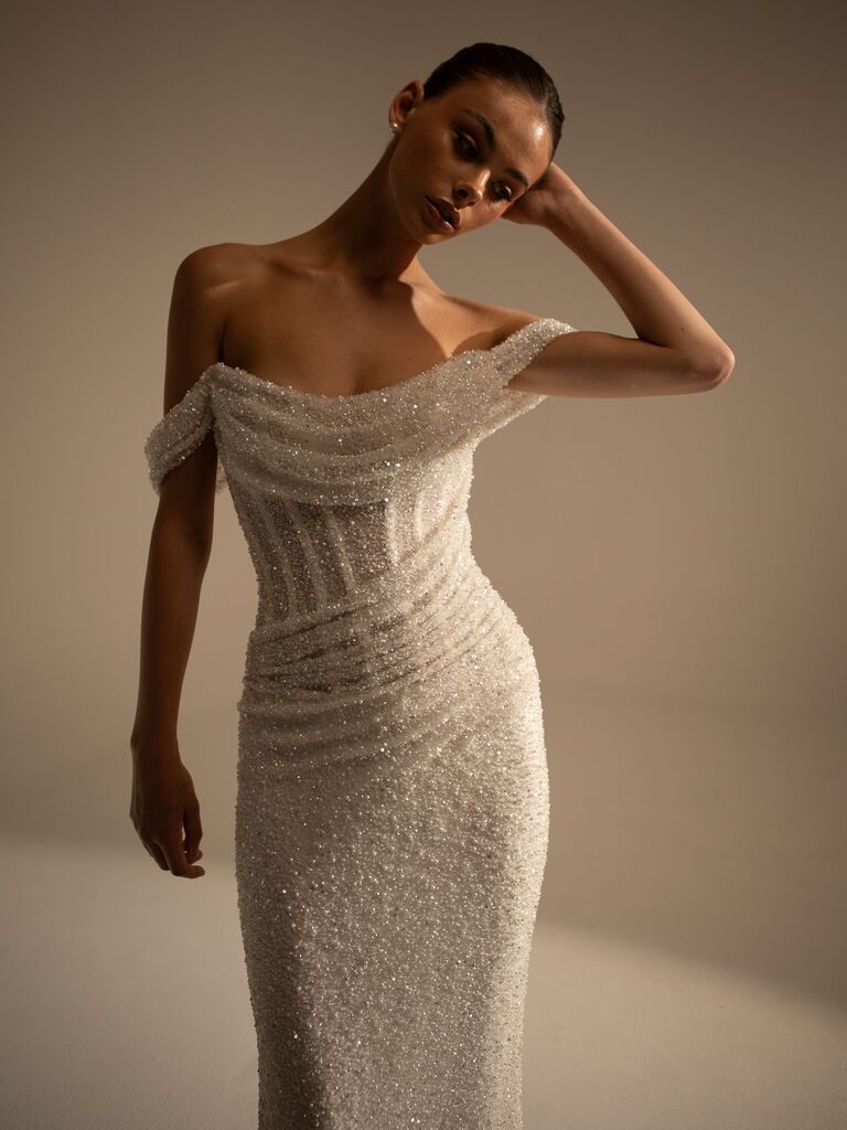 Model wears a sparkling off-the-shoulder white wedding gown. 