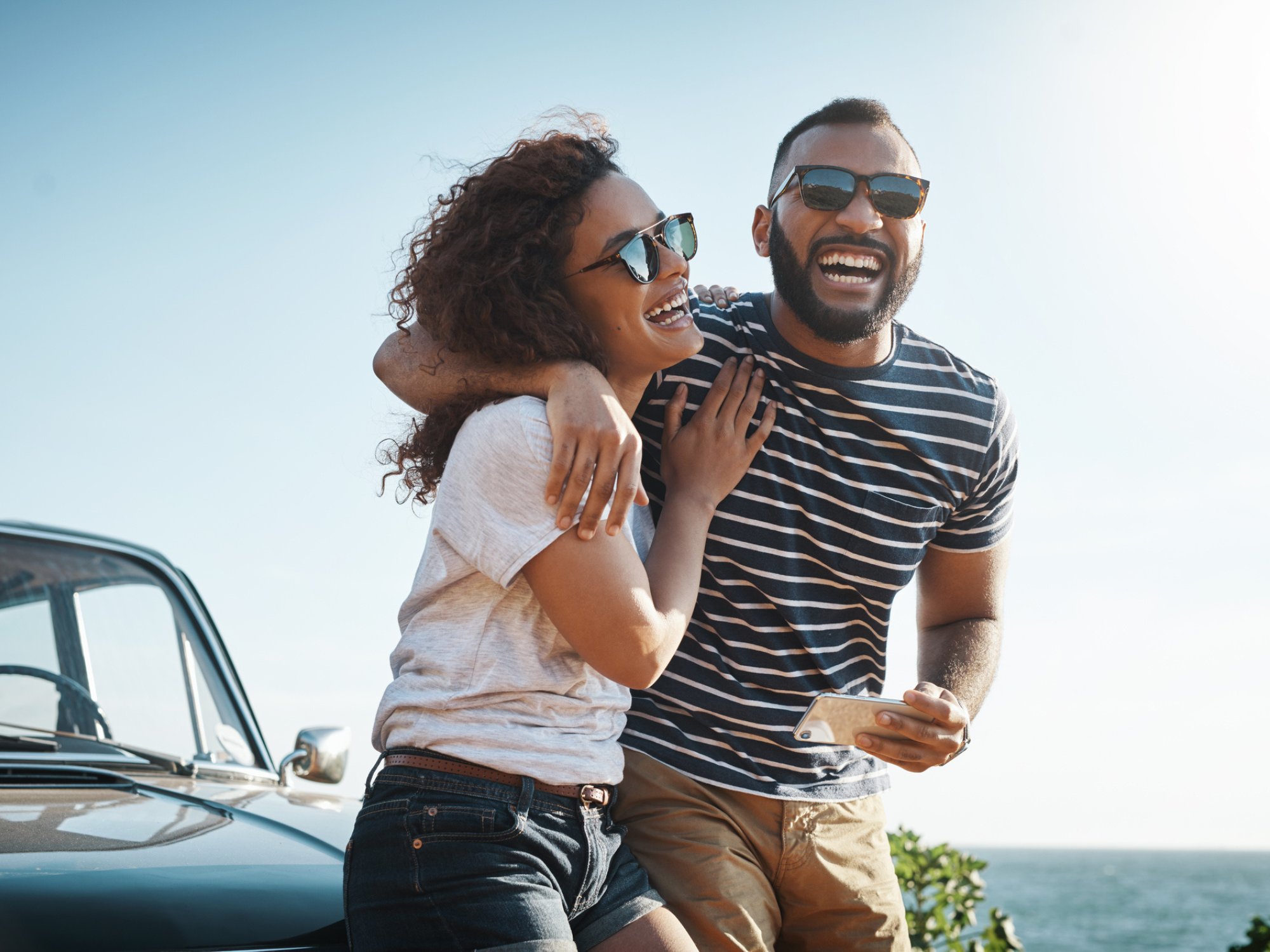 Couple laughing with each other sitting on hood of car