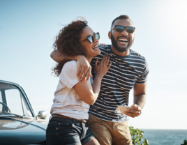 Couple laughing with each other sitting on hood of car