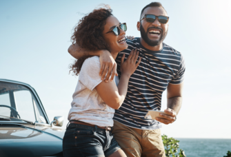 Couple laughing with each other sitting on hood of car